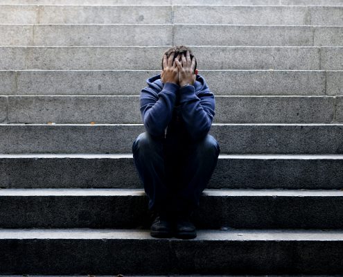 Young homeless man sad crying in depression on ground street